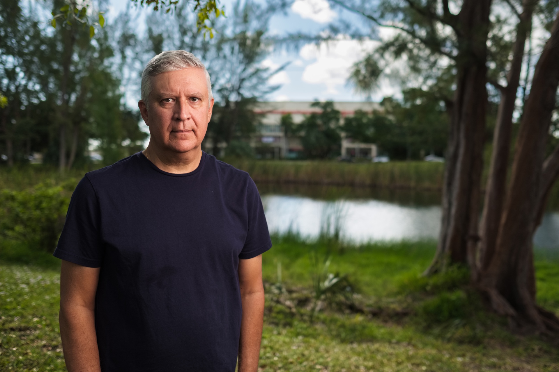 Silver-haired man standing beside a small neighborhood pond on a summer afternoon