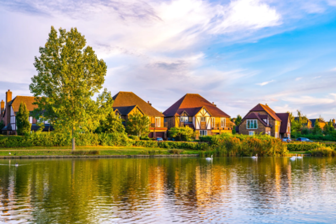 Lakefront homes and docks along a grassy shoreline, reflected in calm golden light