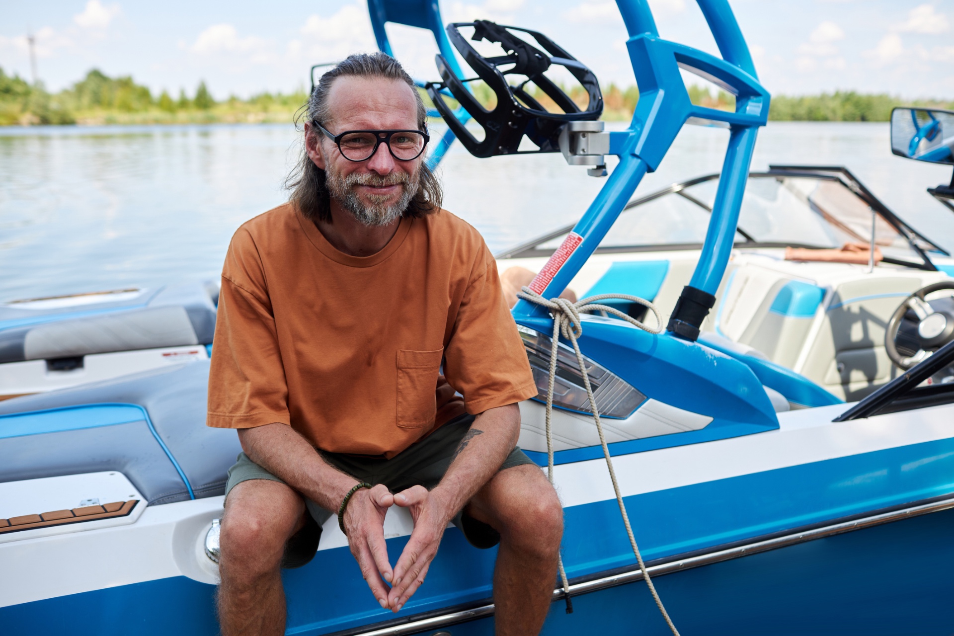 Man at the wheel of a pontoon boat crossing a forested lake