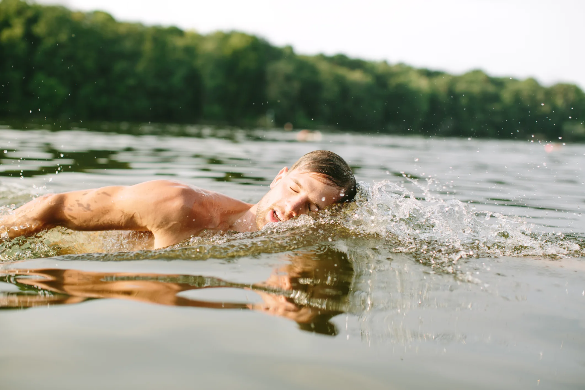 Swimmer mid-stroke in open lake water, treeline behind