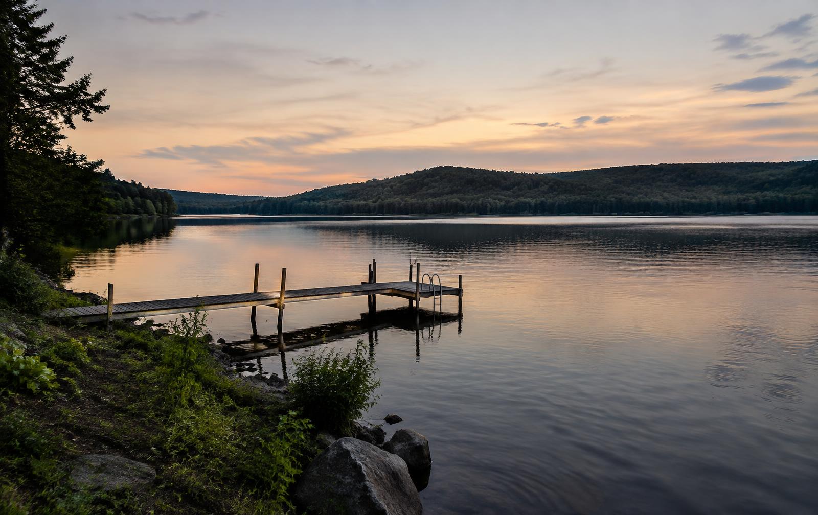 A private wooden dock and natural shoreline on a calm lake at dusk